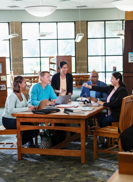 Group of teachers gathered around a table in school library sharing ideas Group of teachers gathered around a table in school library sharing ideas